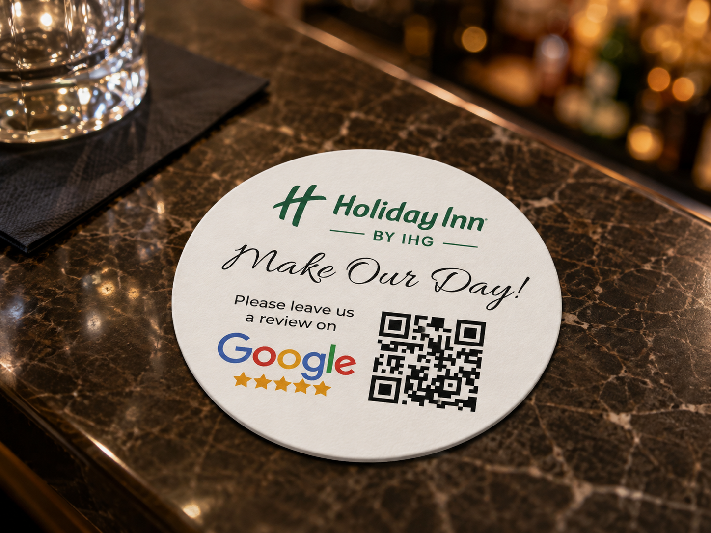Round personalised Holiday Inn coaster displayed on a hotel bar table, featuring branding, a Google review request and a QR code.